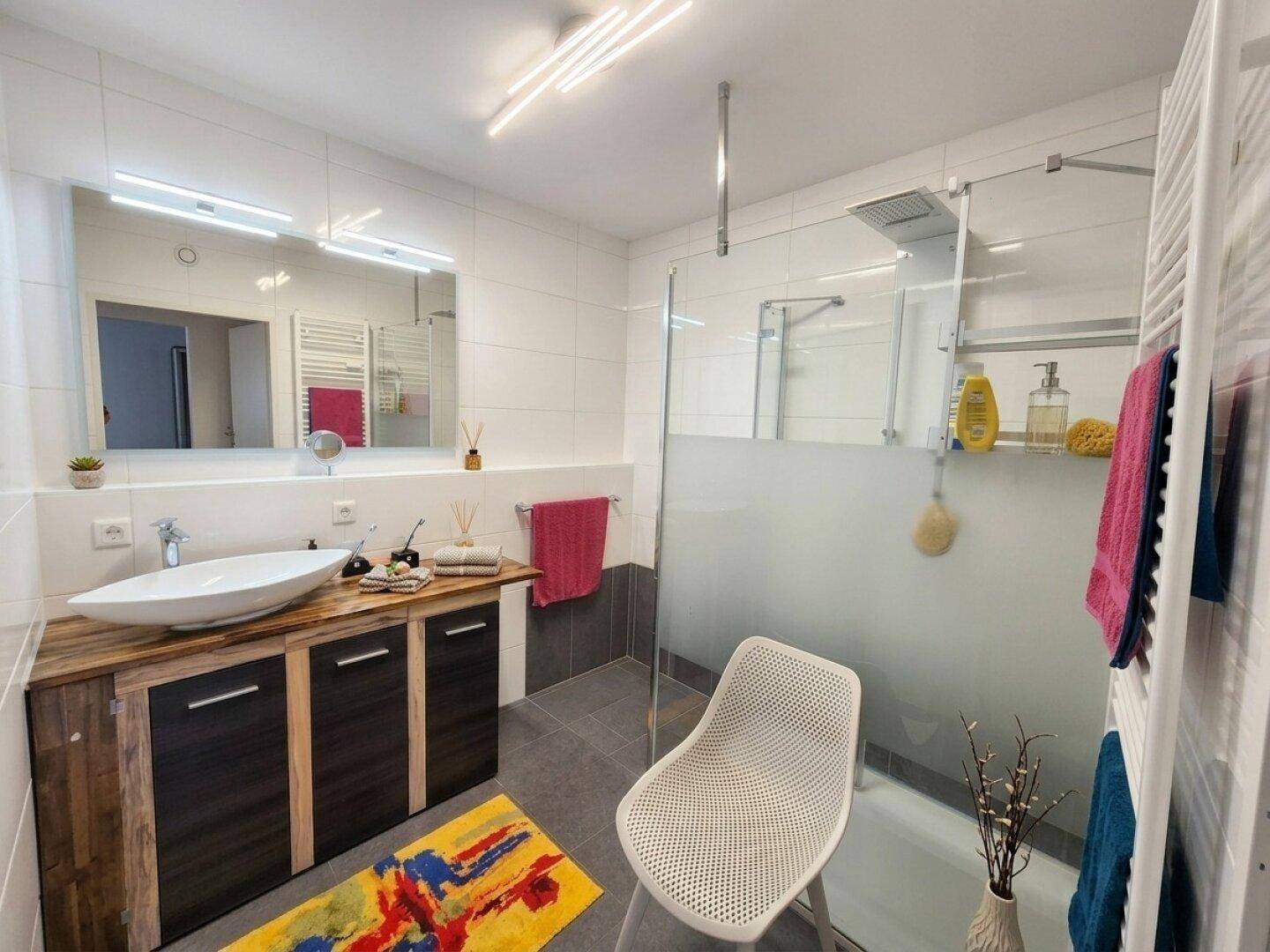 Modernes Badezimmer mit großer Dusche, Holzwaschtisch und beheiztem Handtuchhalter.
