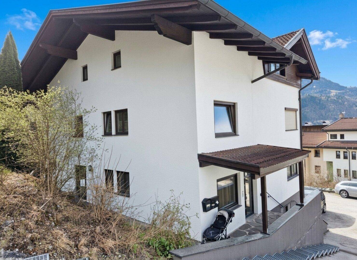 Seitenansicht eines Wohnhauses mit weißer Fassade, Satteldach und Eingangsbereich.