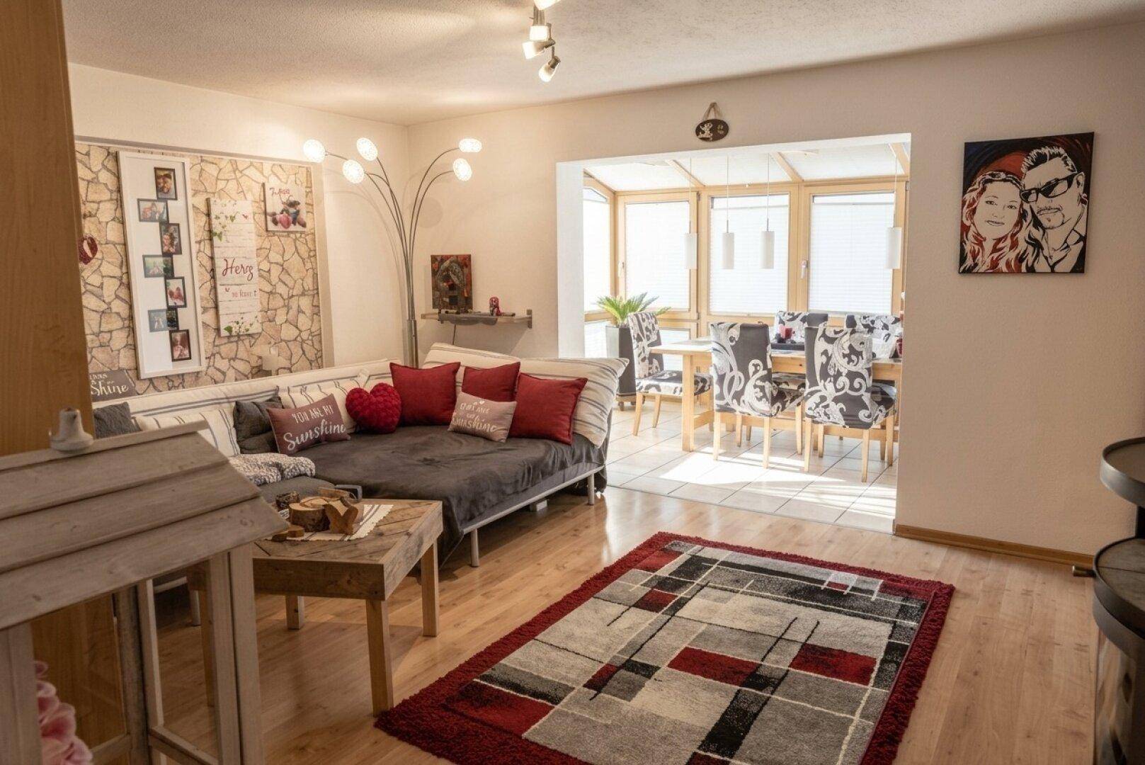 Gemütlicher Wohn-Essbereich mit Holzboden, Kaminofen und Zugang zu einem hellen Wintergarten.