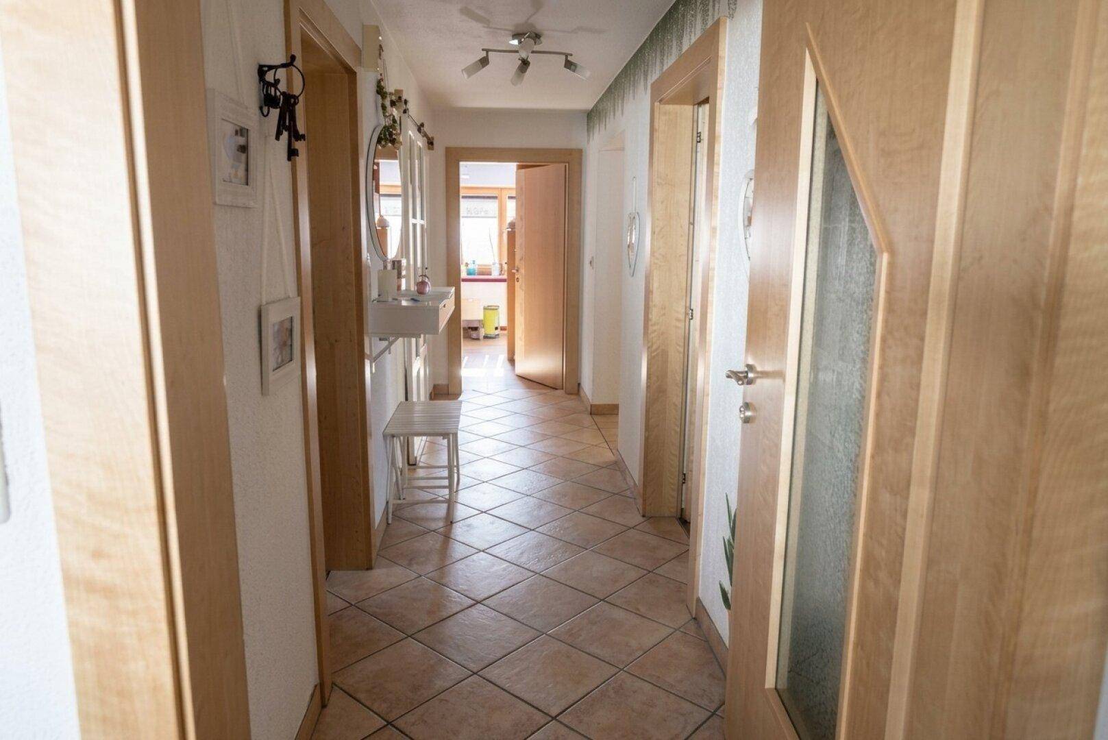 Heller Flur mit Fliesenboden, Holzrahmen und mehreren Türen, die zu anderen Räumen führen.