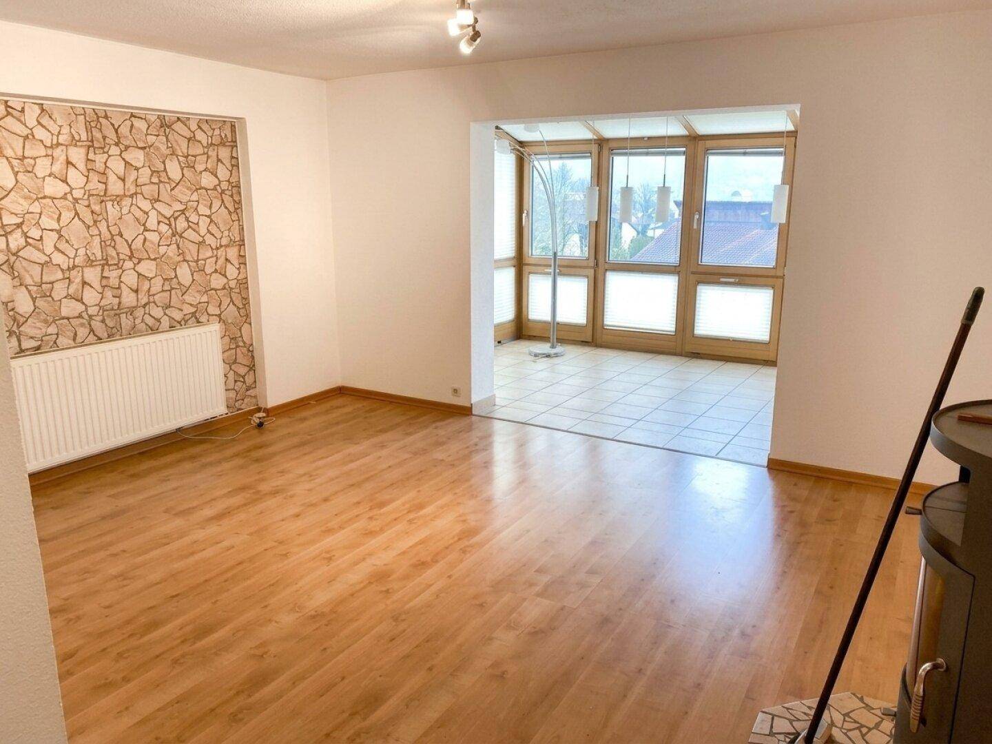 Helles Wohnzimmer mit Laminatboden, Steinwandakzent und Zugang zu einem Wintergarten.