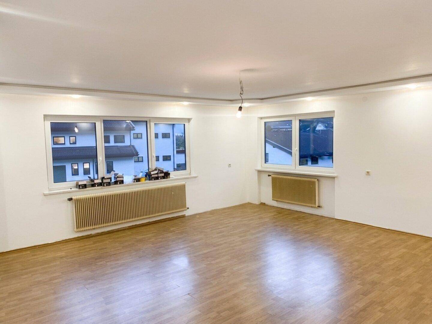 Geräumiges, unmöbliertes Wohnzimmer mit Laminatboden und großen Fenstern.