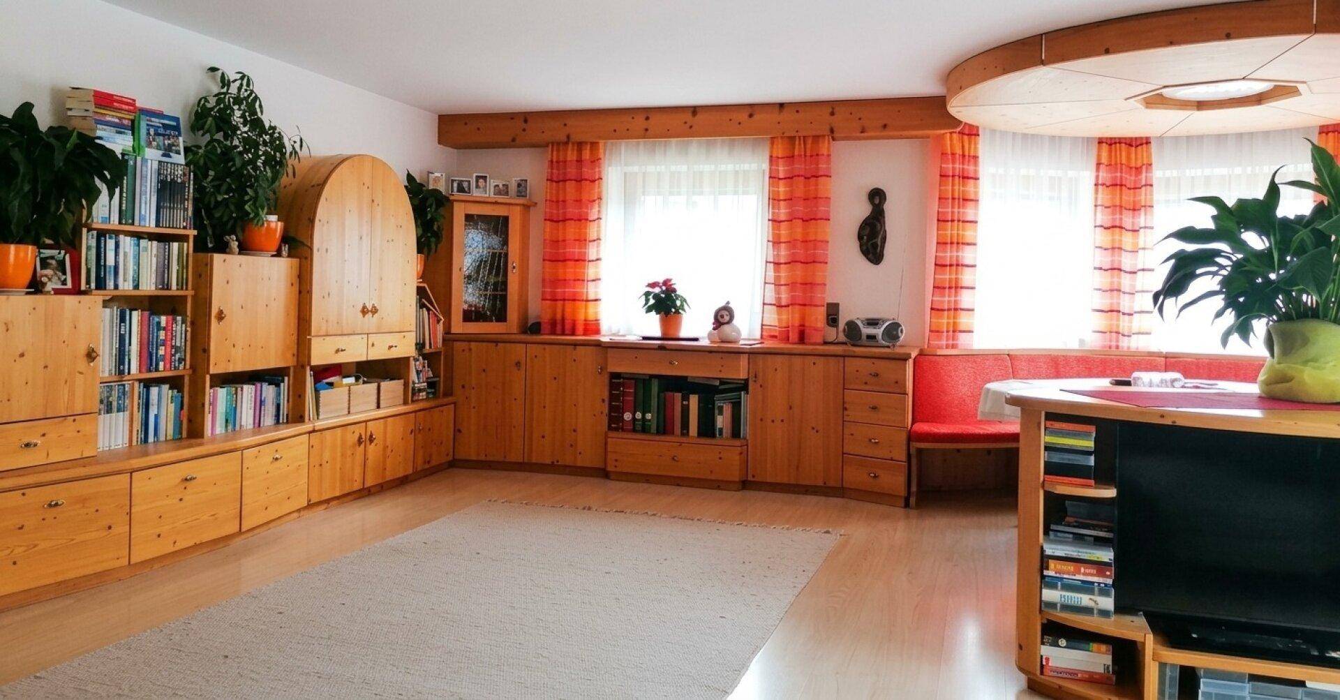 Helles Wohnzimmer mit umfangreichen Holzmöbeln, Bücherregalen und großen Fenstern.