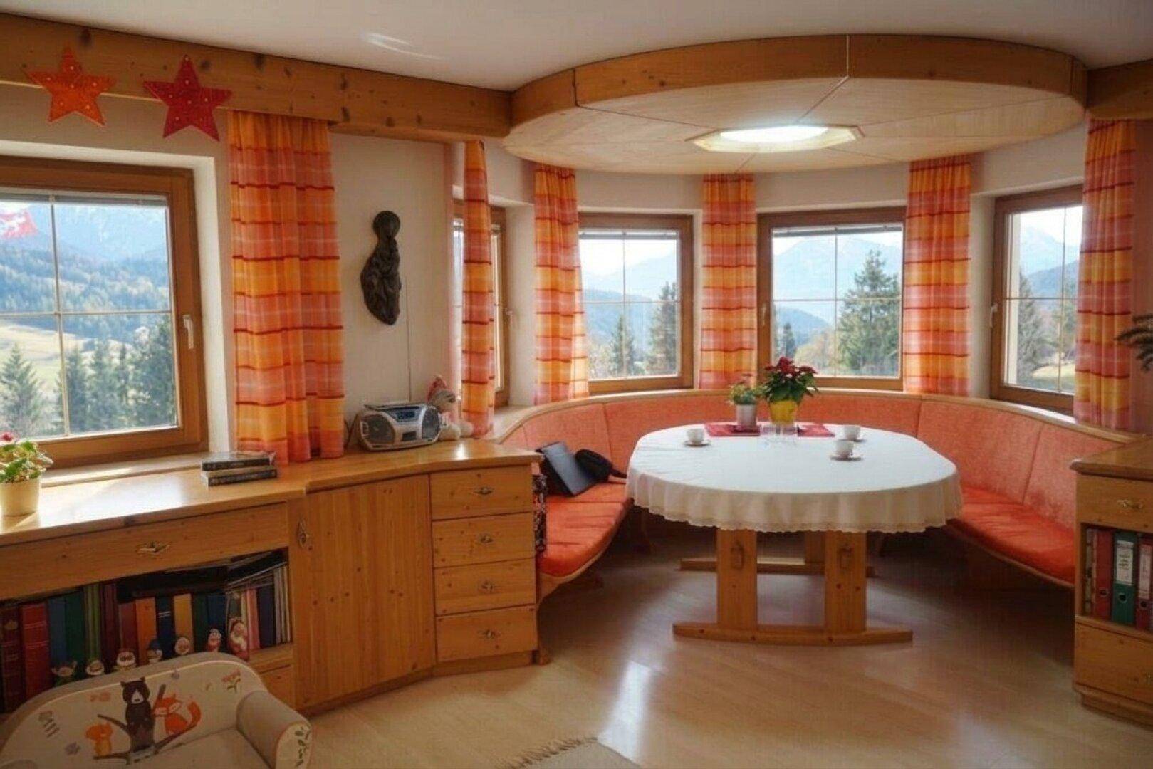 Heller Essbereich mit runder Sitzbank, Holzelementen und Panoramablick auf die Berge.
