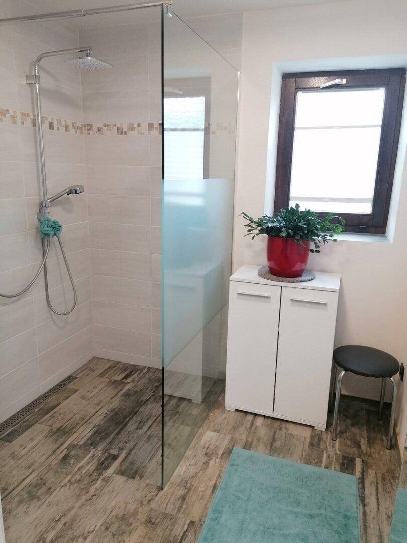 Helles Badezimmer mit ebenerdiger Dusche, Fenster und modernen Fliesen.