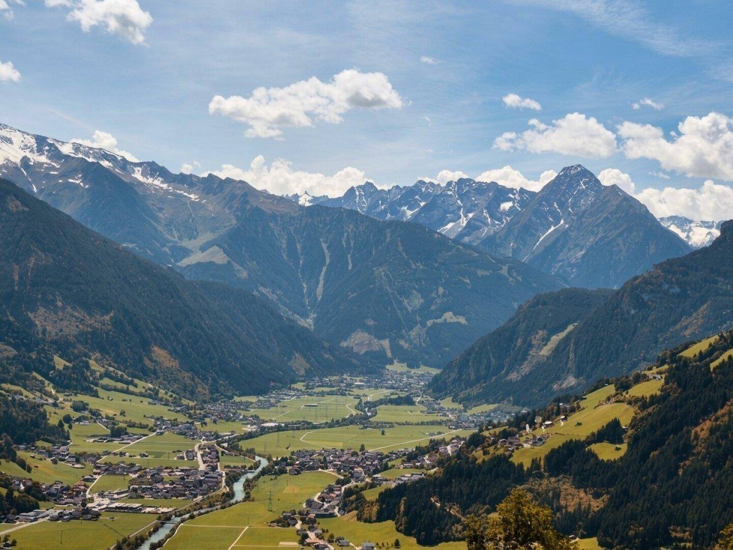 Atemberaubender Panoramablick über ein grünes Tal mit Dorf und majestätischen schneebedeckten Bergen.