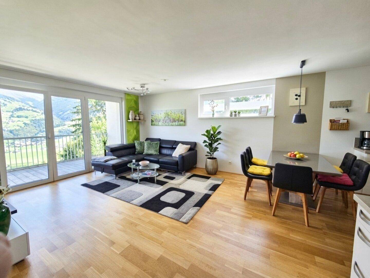 Helles Wohn-Esszimmer mit Holzboden, moderner Einrichtung und Zugang zu einem Balkon mit Bergblick.