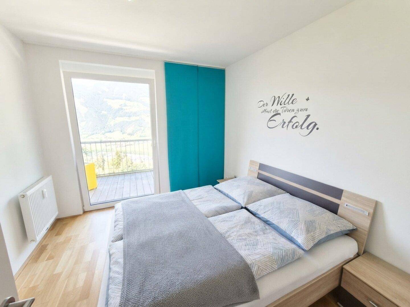 Helles Schlafzimmer mit Holzboden, Balkonzugang und inspirierendem Wandtattoo.