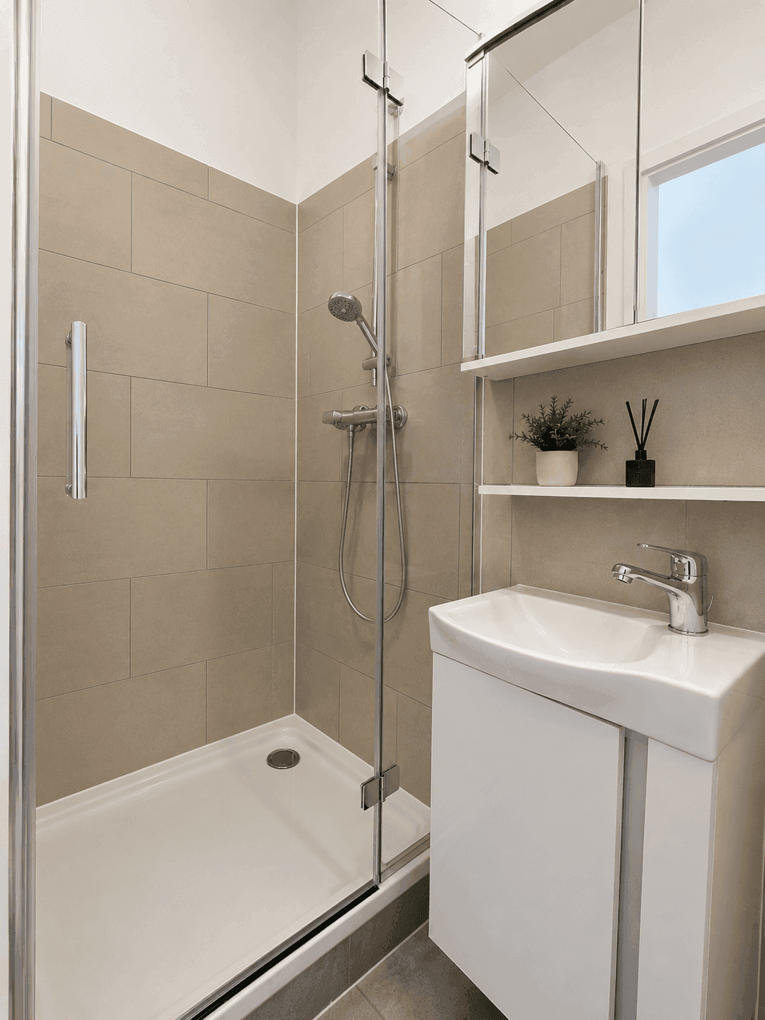 Modernes Badezimmer mit Duschkabine, Waschbecken und beigefarbenen Fliesen.