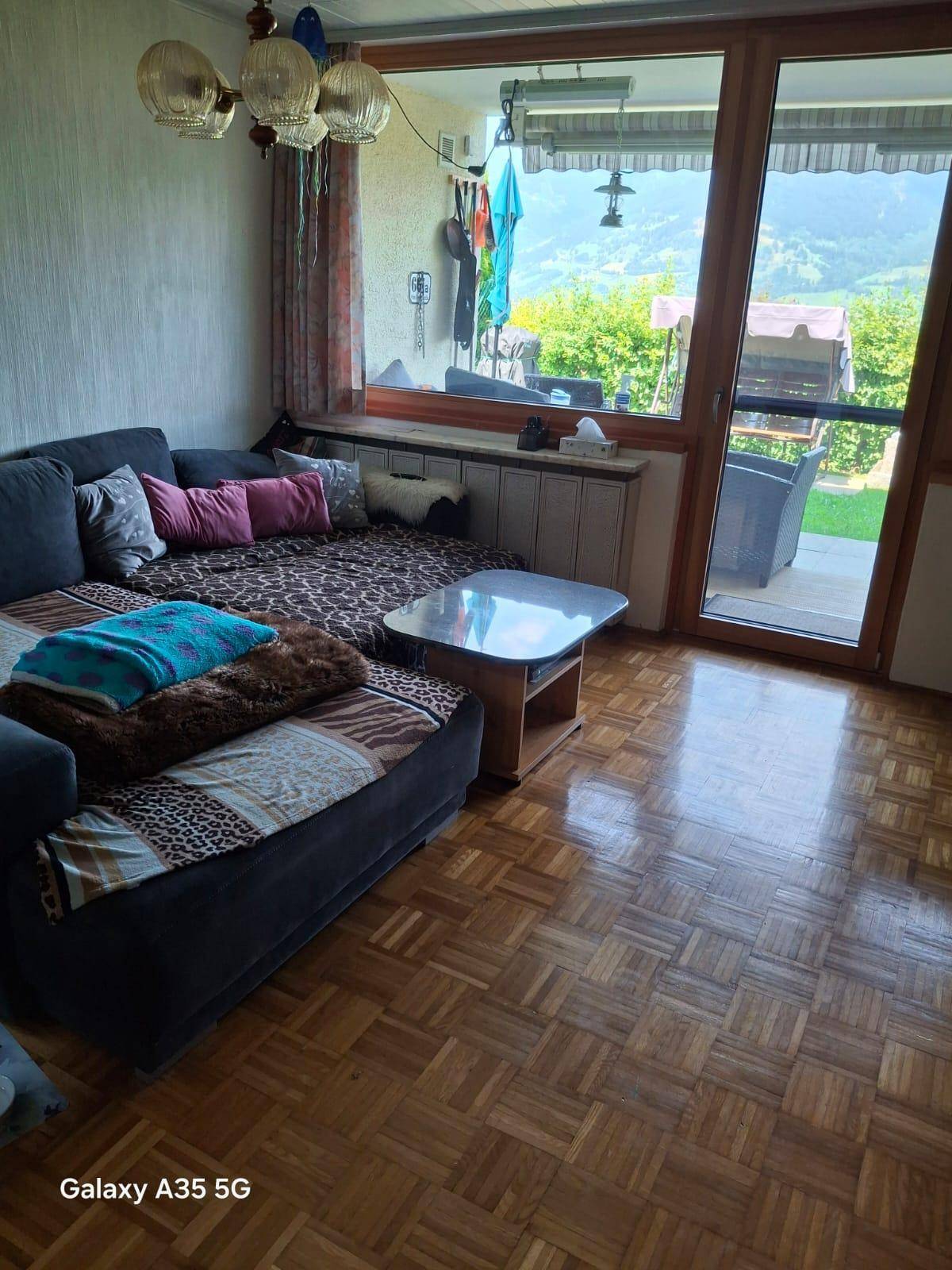Gemütliches Wohnzimmer mit Parkettboden, großem Sofa und Zugang zu einem Balkon mit Bergblick.