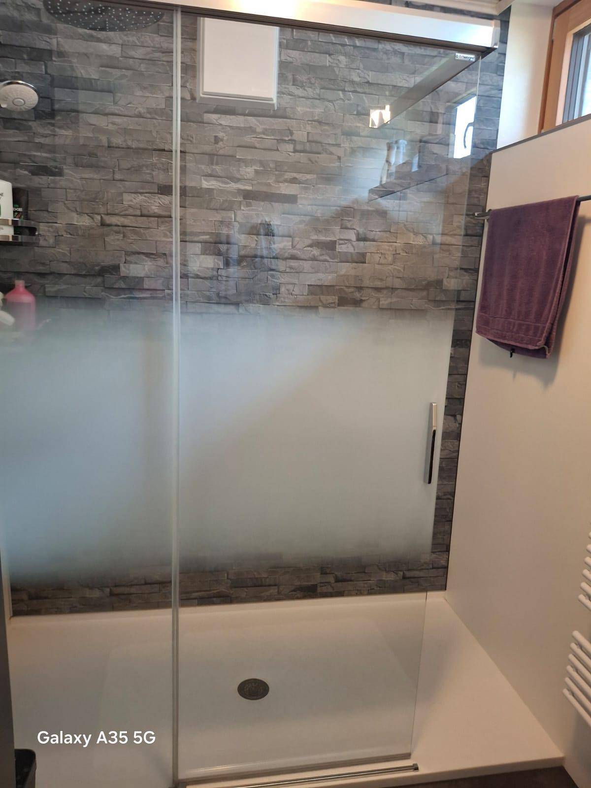 Duschbereich mit Glasabtrennung und dekorativen Steinwandfliesen im modernen Badezimmer.