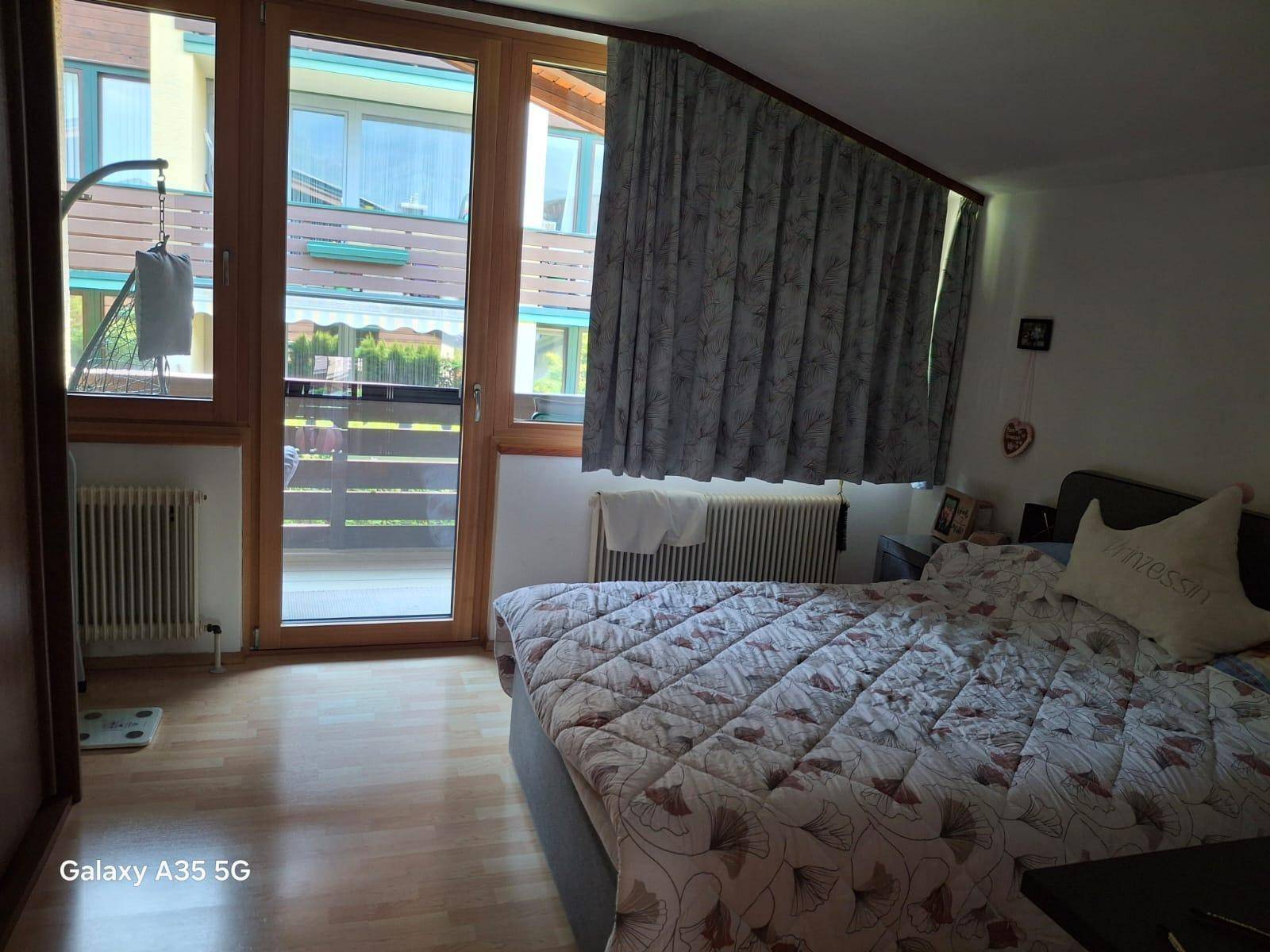 Schlafzimmer mit Holzboden, Doppelbett und direktem Zugang zu einem sonnigen Balkon.
