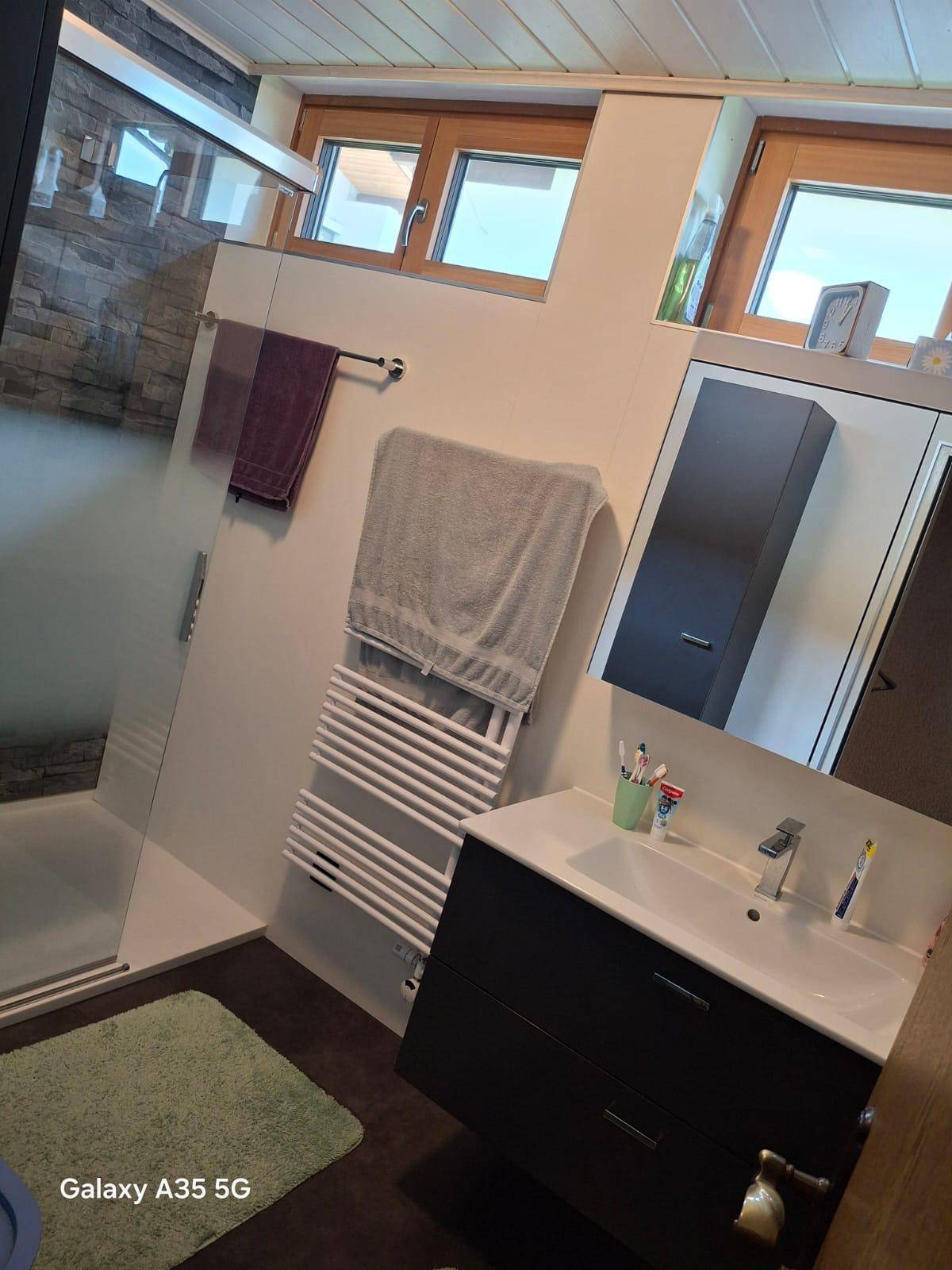 Modernes Badezimmer mit Waschtisch, beheiztem Handtuchhalter und Duschbereich mit Steinoptikfliesen.