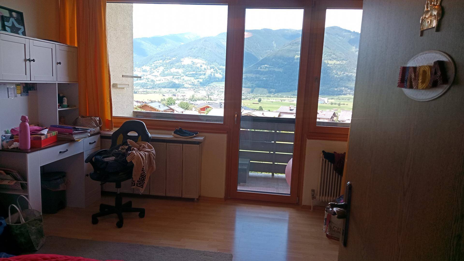 Helles Zimmer mit Schreibtisch, Holzboden und weitem Bergblick vom Balkon.