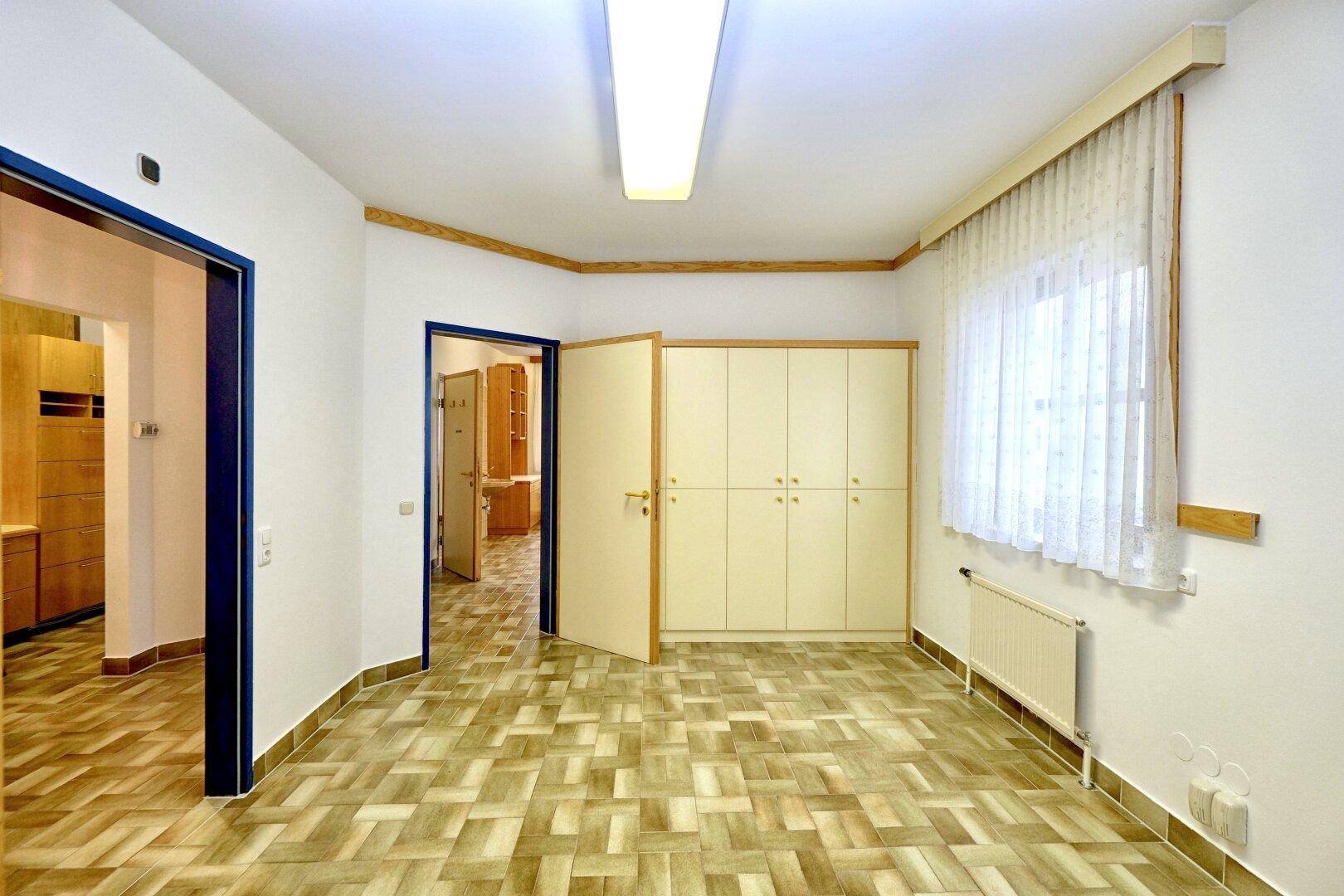 Heller Büroraum mit Einbauschränken, einem Fenster und gemustertem Fliesenboden.
