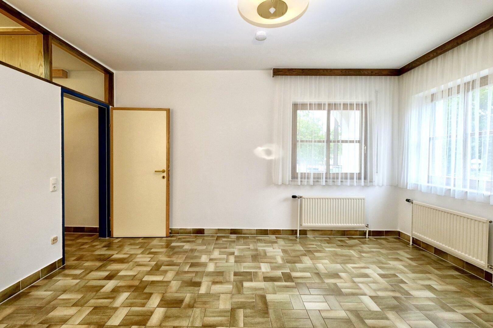 Leerer Raum mit großen Fenstern, Heizkörpern und einem gemusterten Fliesenboden.