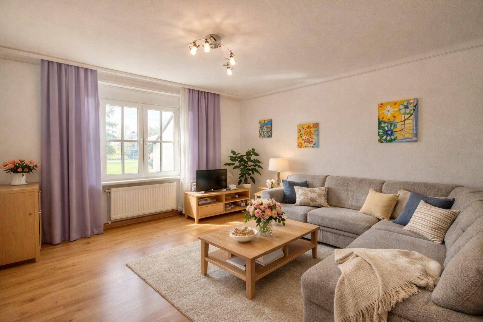 Helles Wohnzimmer mit Holzboden, bequemer Couch und farbenfrohen Bildern an der Wand.