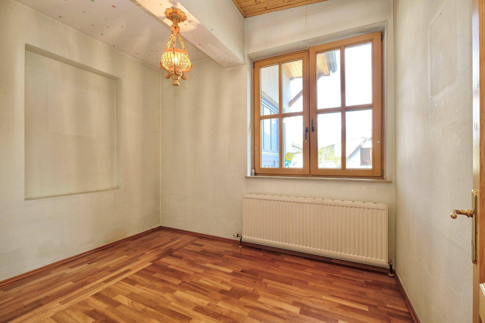 Kleiner Raum mit Holzboden, Fenster und einer Deckenlampe, ideal als Kinder- oder Arbeitszimmer.