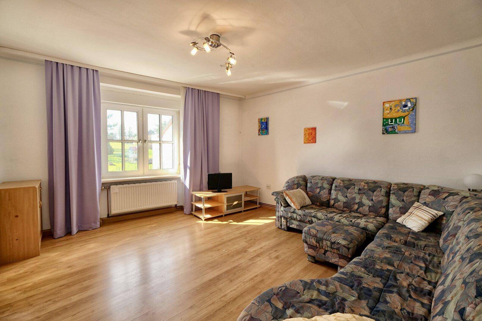 Wohnzimmer mit Holzboden, großem Sofa und farbenfrohen Kunstwerken an den Wänden.