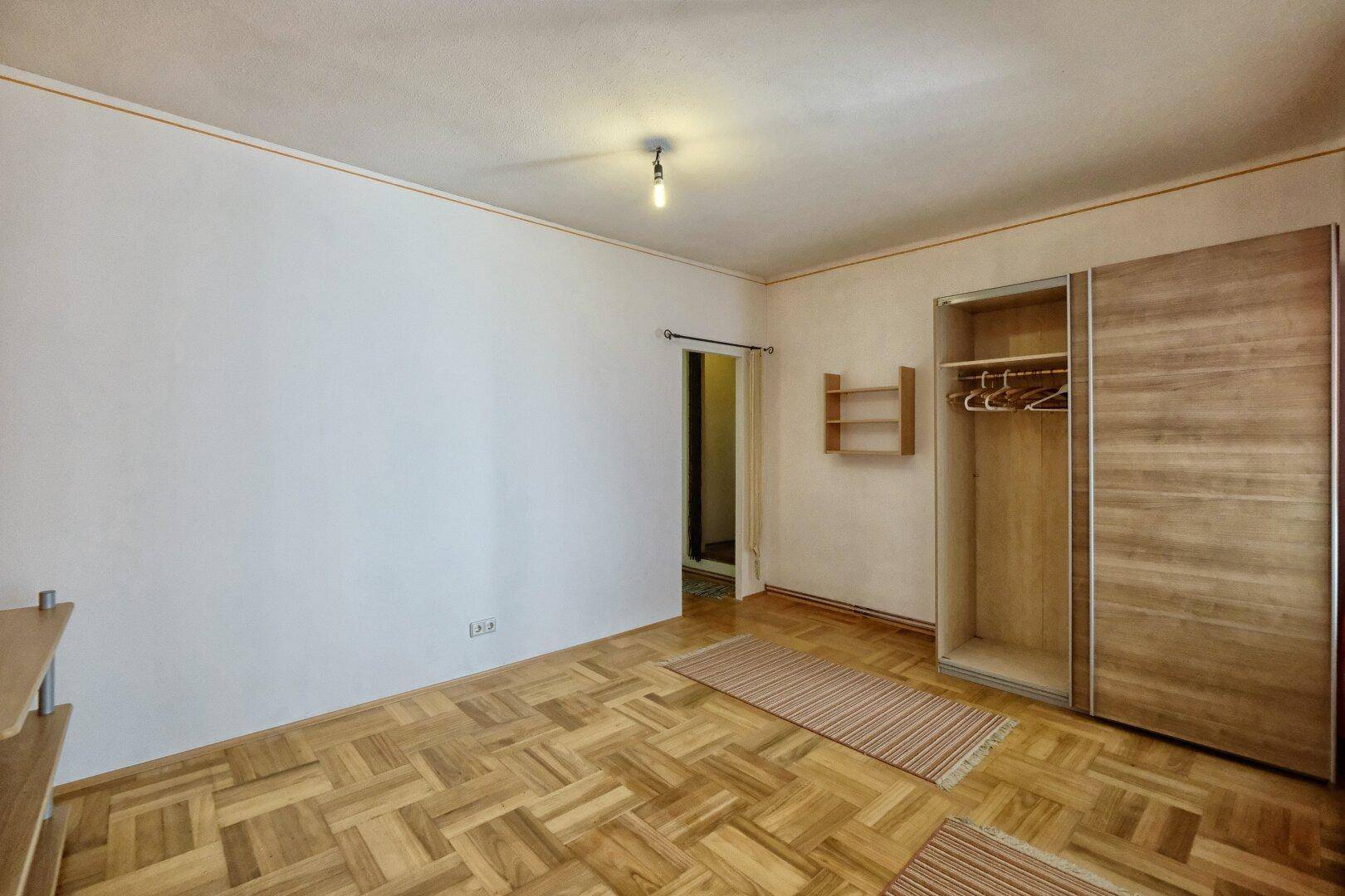 Schlafzimmer mit Holzboden, offenem Kleiderschrank und viel Platz für individuelle Gestaltung.