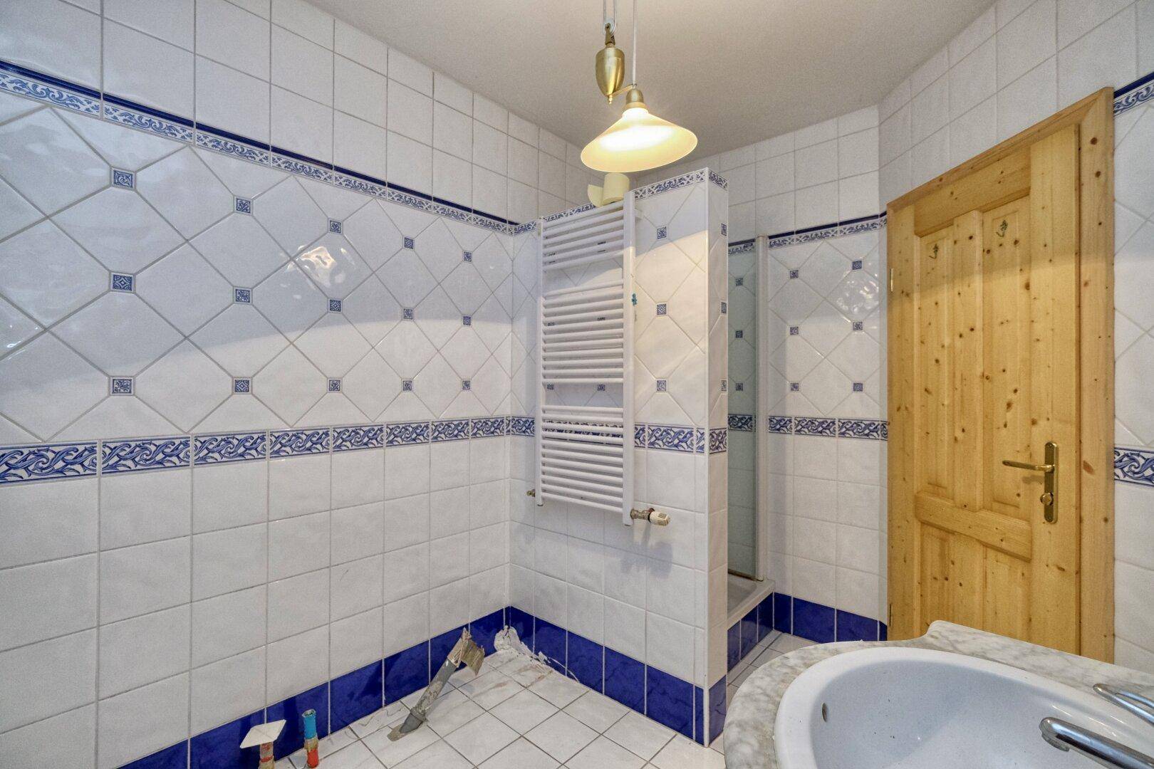 Badezimmer mit weiß-blauen Fliesen, Duschbereich und beheiztem Handtuchhalter.