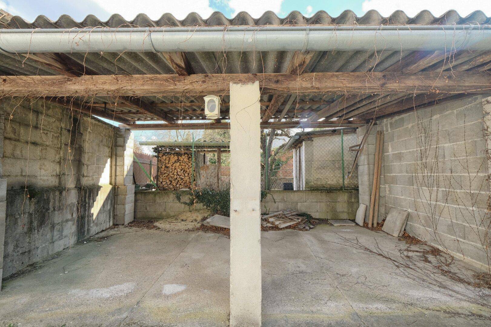 Einfacher Carport mit Betonboden und Holzkonstruktion, ideal für ein Fahrzeug oder als Lagerfläche.