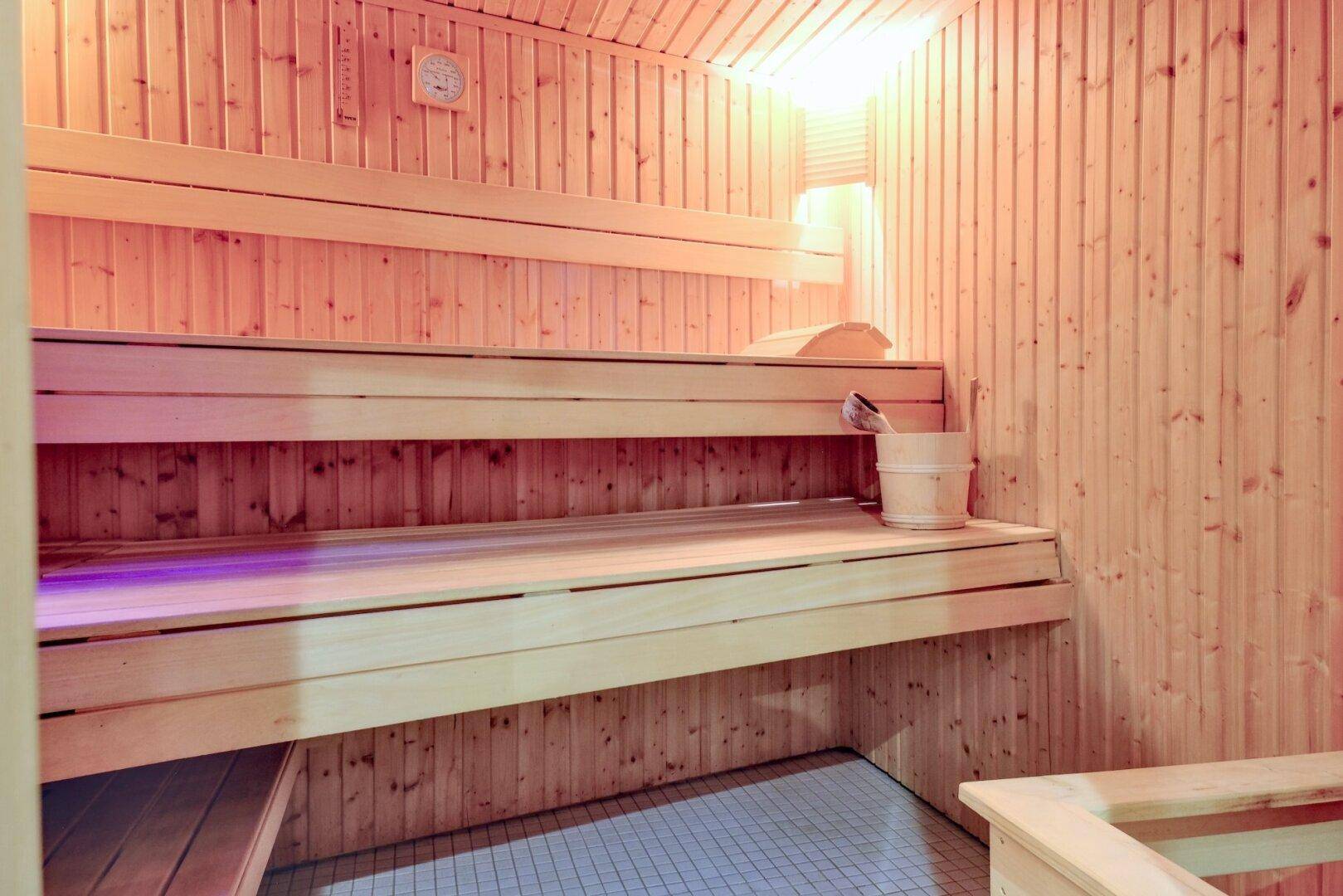 Traditionelle Holzsauna mit mehreren Bänken und einem Eimer für Aufgüsse.