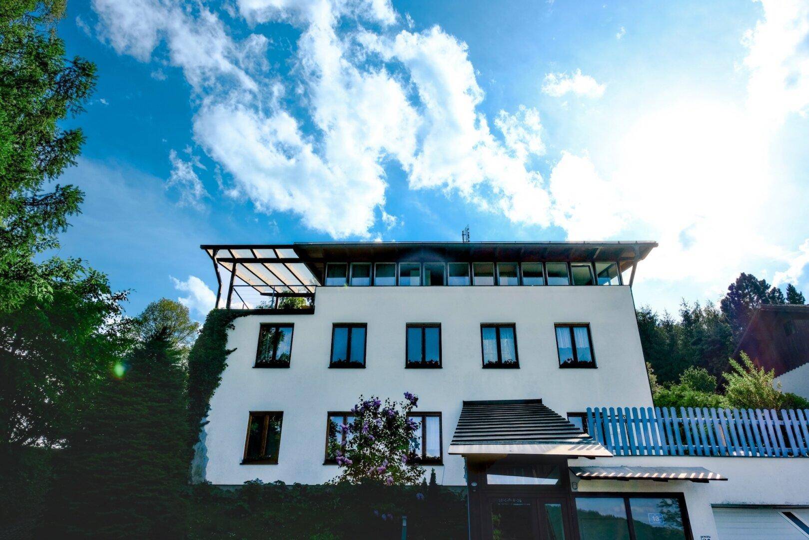 Weißes Mehrfamilienhaus mit vielen Fenstern und einem Balkon unter blauem Himmel.