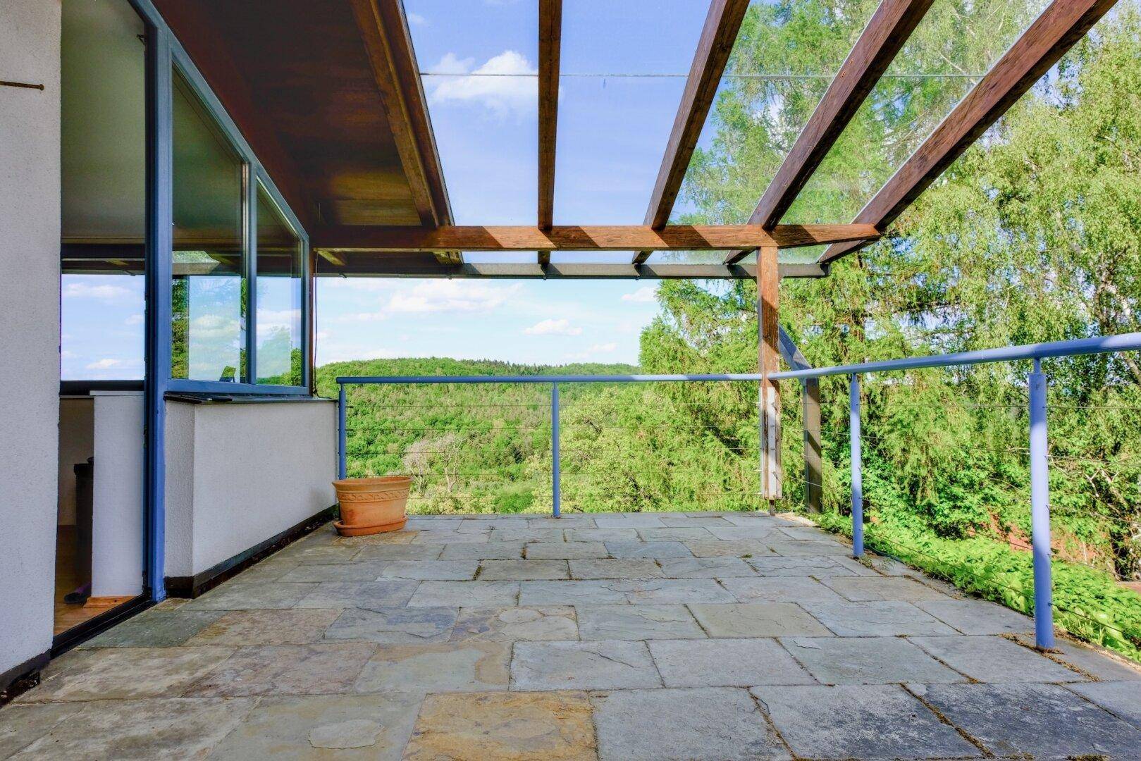 Geräumige Terrasse mit Steinfliesen und weitem Blick über die grüne Landschaft.