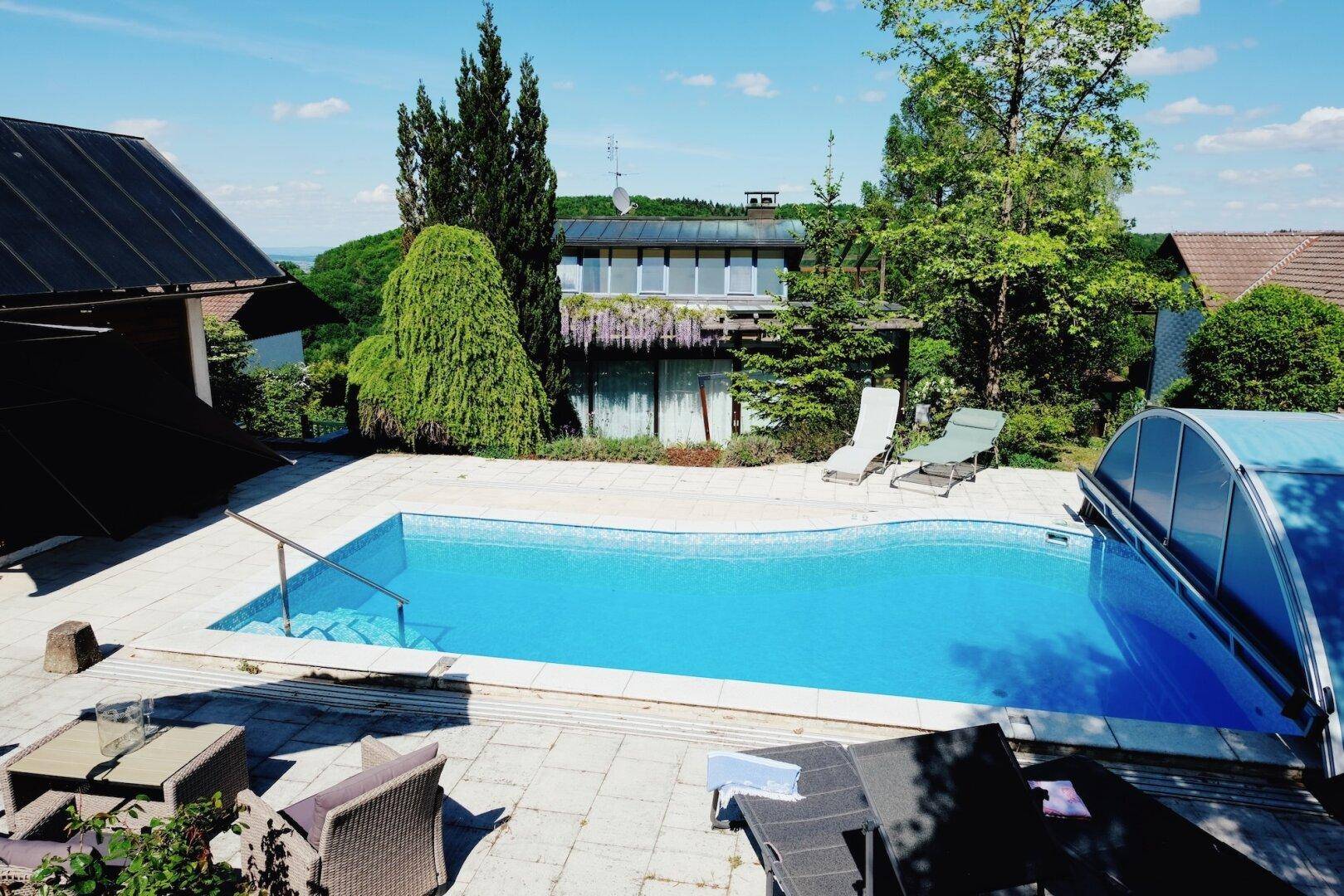 Außenbereich mit großem Swimmingpool, Liegestühlen und Blick auf das Haus.