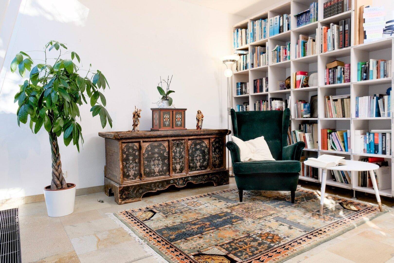 Gemütliche Bibliothek mit großem Bücherregal, Sessel und orientalischem Teppich.