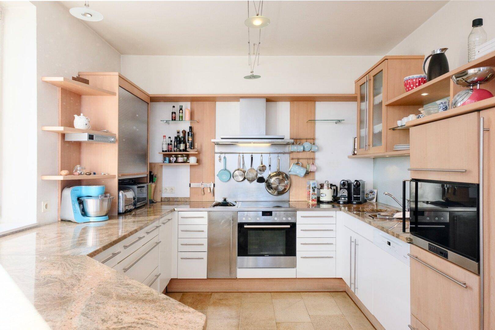 Moderne Einbauküche mit hellen Holzfronten, Granitarbeitsplatten und integrierten Geräten.