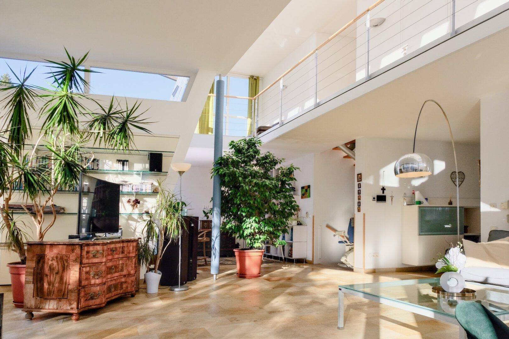 Helles, offenes Wohnzimmer mit hohen Decken, Galerie und vielen Pflanzen.