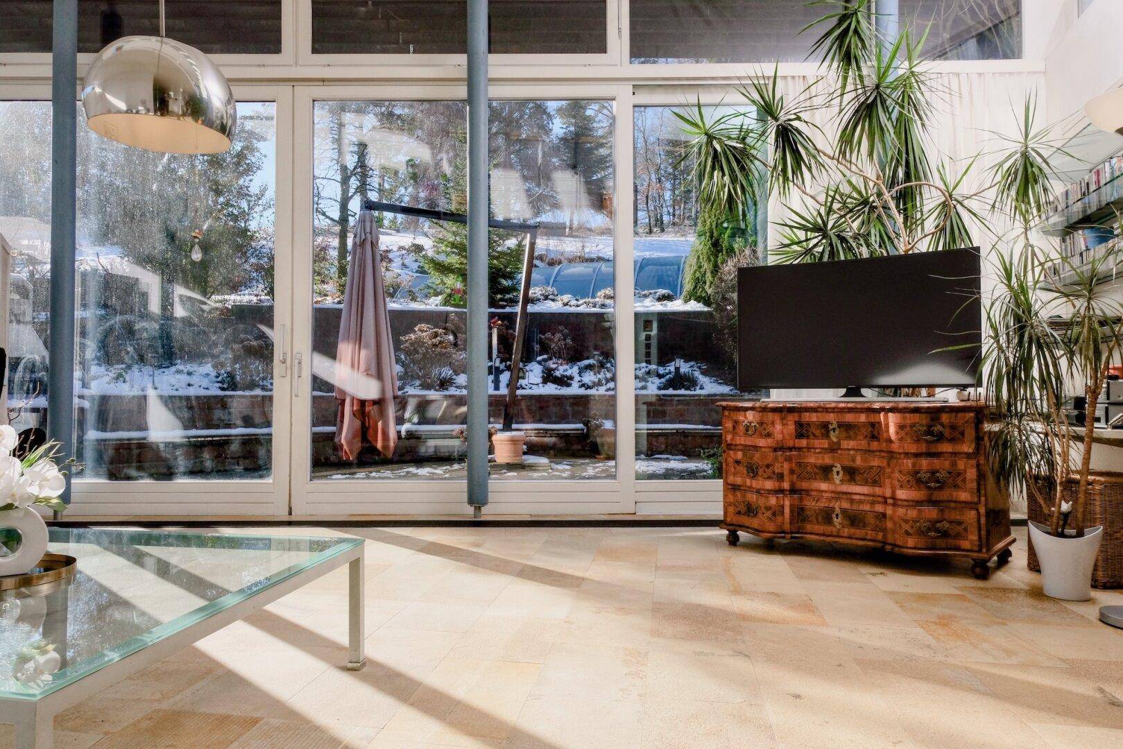 Heller Wohnbereich mit großen Fenstern, Blick in den verschneiten Garten und Steinfliesenboden.