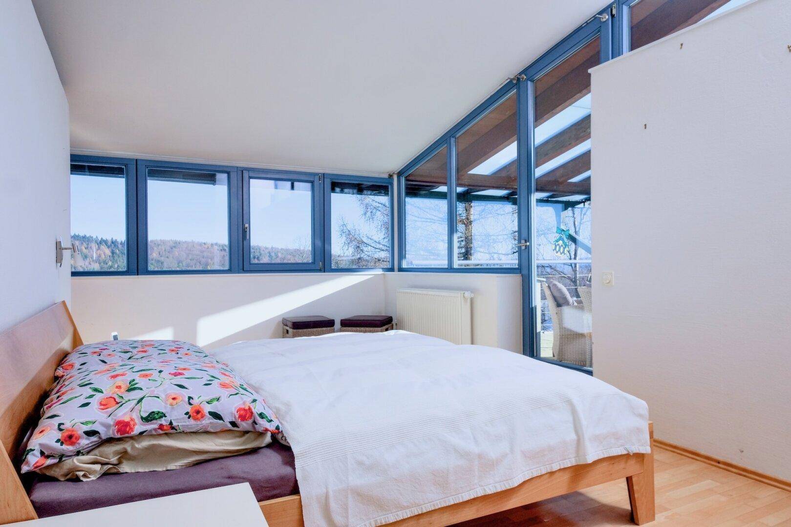 Schlafzimmer mit Holzbett, großen Fenstern und Zugang zu einem Außenbereich.