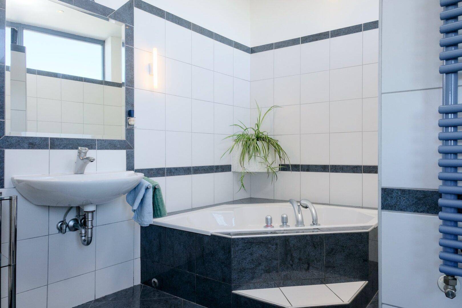 Badezimmer mit Eckbadewanne, Waschbecken und blauen Akzenten in den Fliesen.