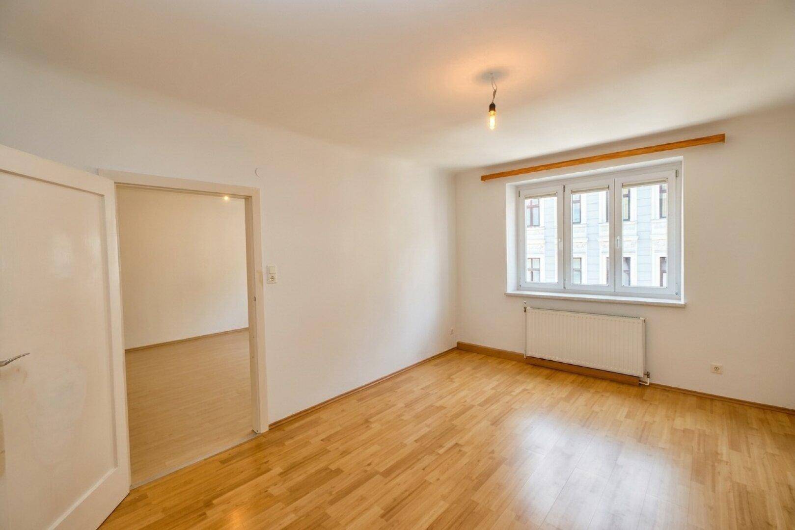 Leerer Raum mit Holzboden, weißen Wänden und Blick auf die umliegenden Gebäude.