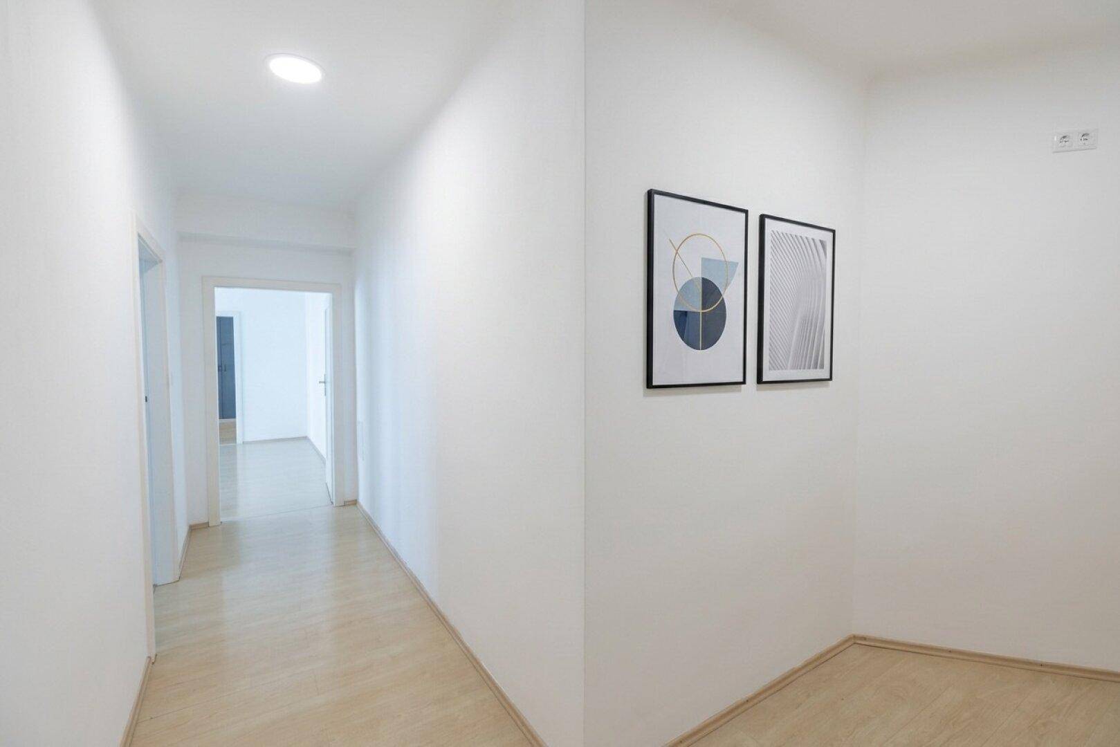 Langer, heller Flur mit Holzboden und modernen Wandbildern.