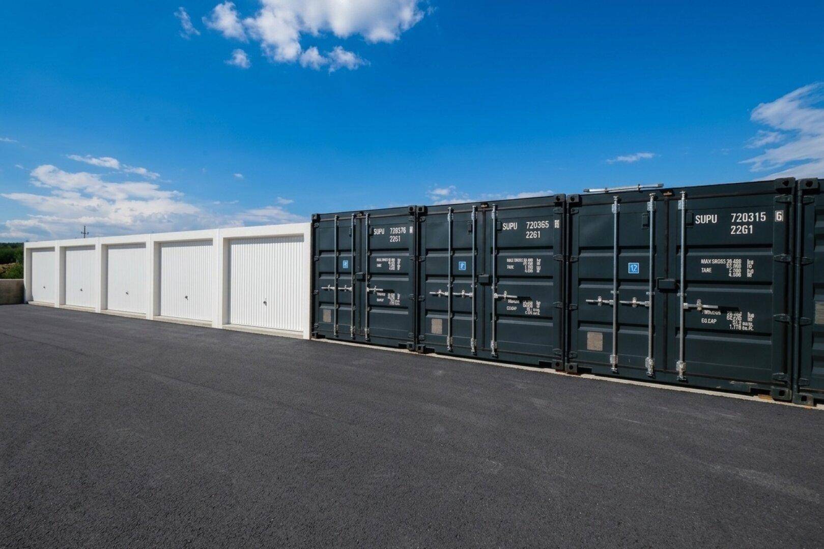Reihe von weißen Lagergaragen und dunklen Schiffscontainern unter klarem blauem Himmel.
