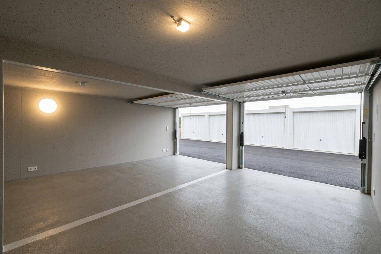 Geräumige, leere Lagergarage mit Betonboden und geöffnetem Tor, Blick auf weitere Einheiten.