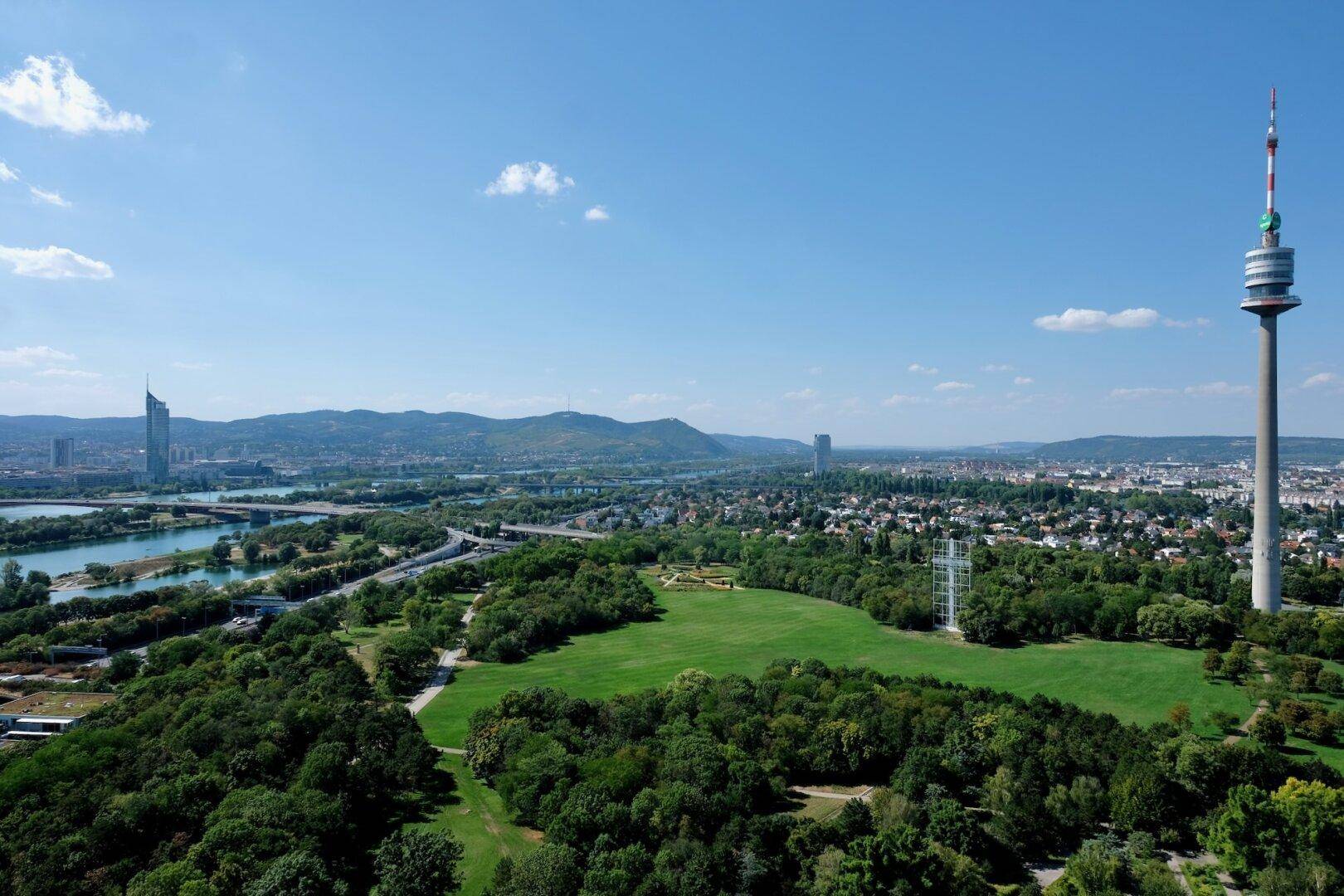 Panoramablick über die Stadt Wien mit Donau, Grünflächen und dem Donauturm.