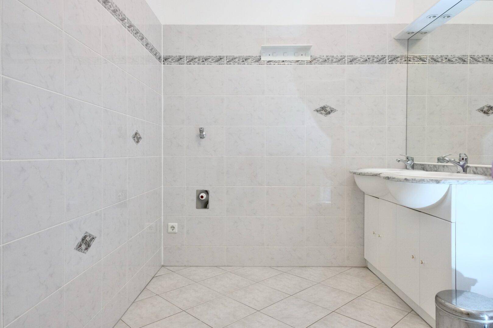 Badezimmer mit weißen Fliesen, Einzelwaschbecken und großem Spiegel.