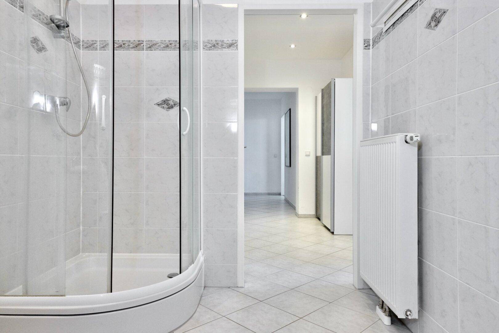 Badezimmer mit Duschkabine, weißen Fliesen und Heizkörper.