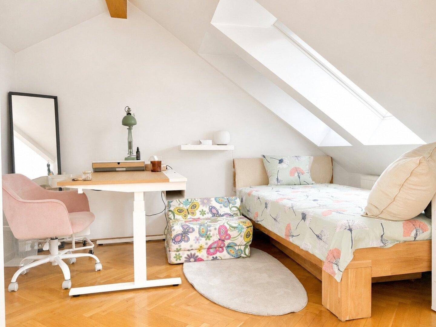 Schlafzimmer mit Dachschräge, Holzbett, Schreibtisch und großem Dachfenster für viel Tageslicht.