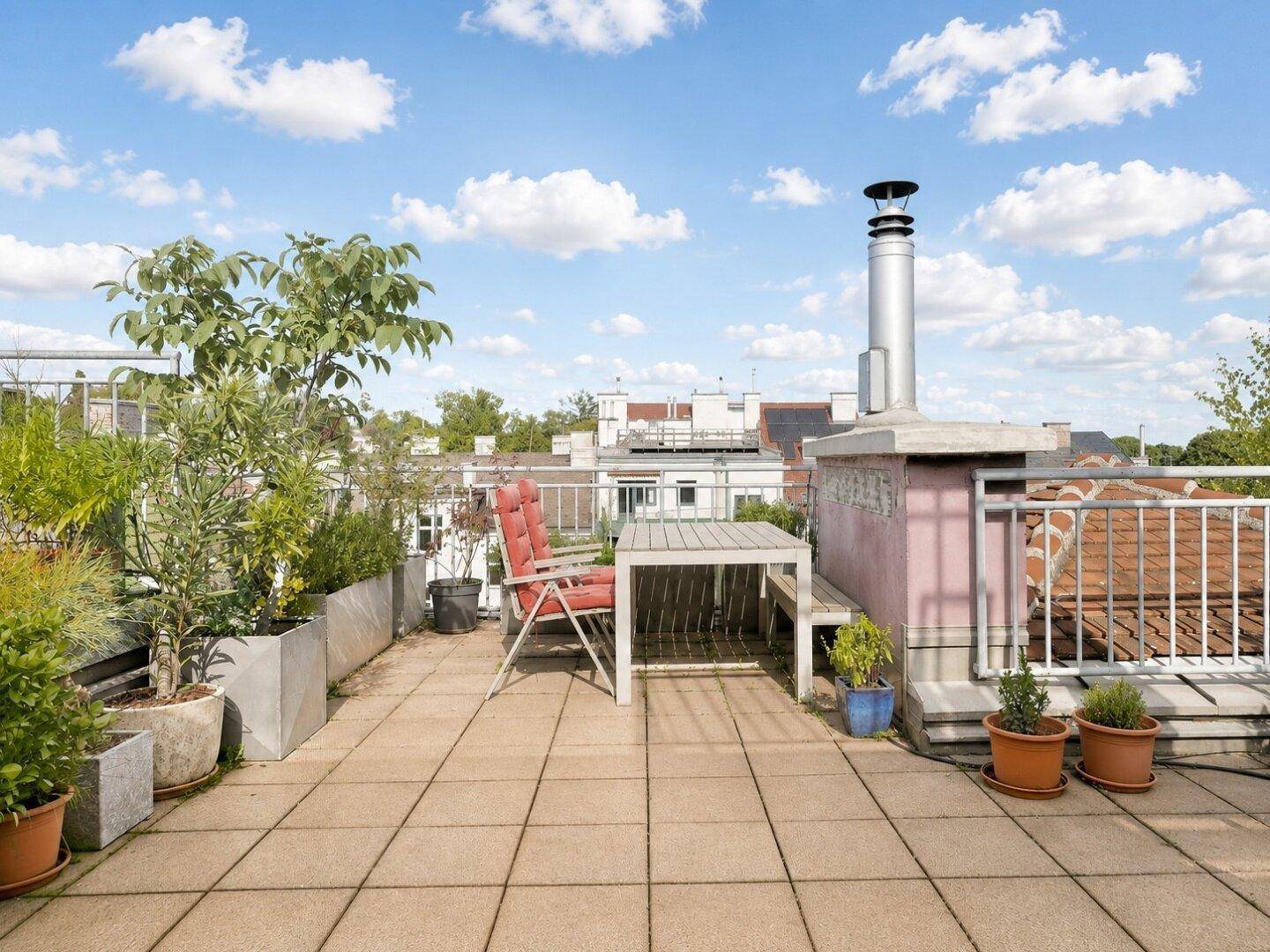 Geräumige Dachterrasse mit Sitzgelegenheiten, Topfpflanzen und weitem Blick über die Dächer der Stadt.