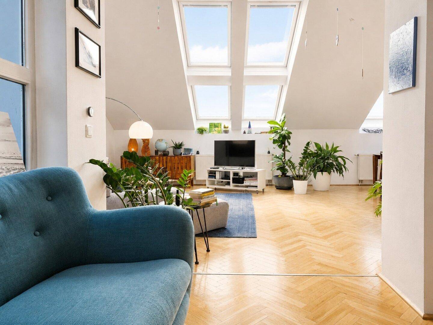 Helles Wohnzimmer mit großen Dachfenstern, Parkettboden und einem blauen Sessel als Farbakzent.