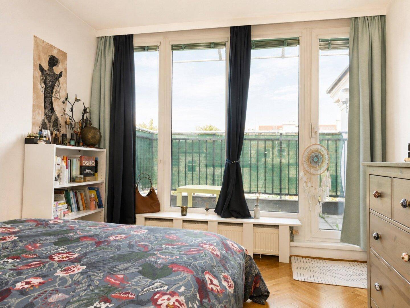 Schlafzimmer mit großem Bett, Bücherregal und bodentiefen Fenstern mit Zugang zu einem Außenbereich.
