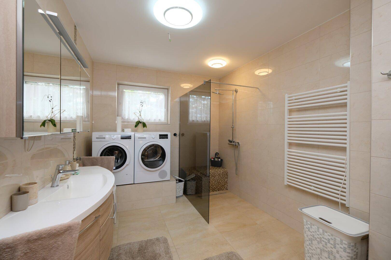 Modernes Badezimmer mit begehbarer Dusche, Waschmaschine und Trockner sowie Fenster.