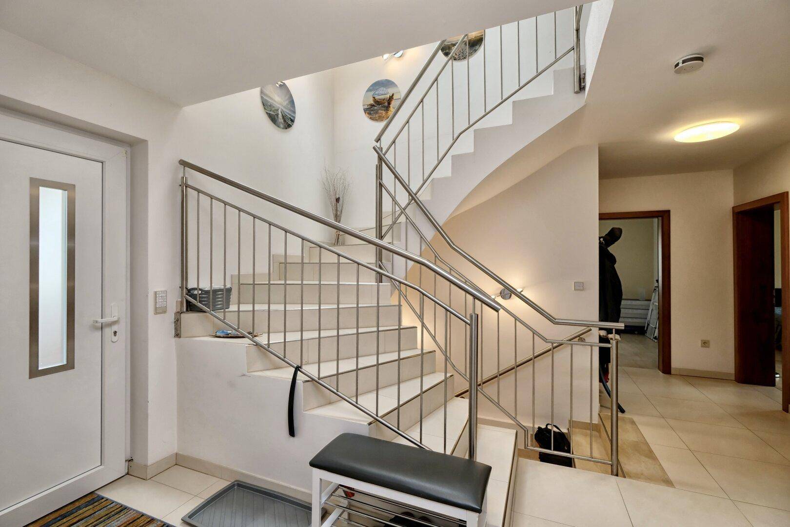 Heller Eingangsbereich mit moderner Treppe aus Edelstahl und Fliesenboden.