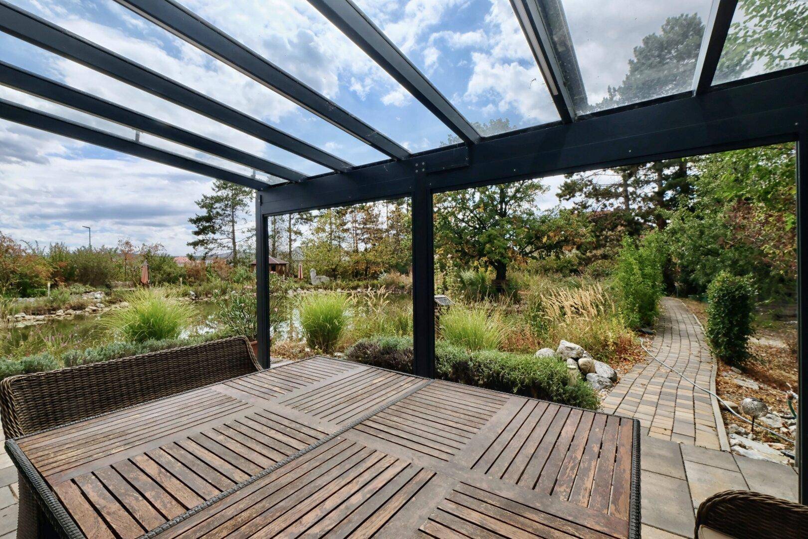 Überdachte Terrasse mit Holztisch und Blick auf den naturnahen Garten mit Teich.